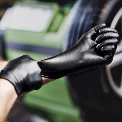 Mãos calçando luvas pretas diante de um carro verde e roda preta