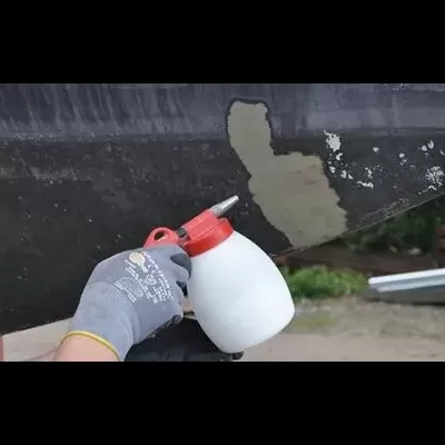 Pulverizador branco com tampa vermelha sendo usado para aplicar produto numa superfície metálica escura