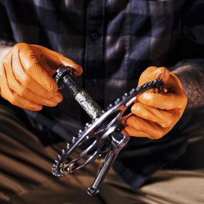 Mãos com luvas laranja segurando peça mecânica metálica com dentes.