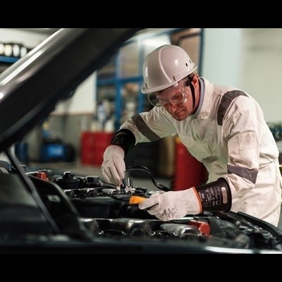 Homem em fato e capacete a reparar motor de carro numa oficina com tambores ao fundo