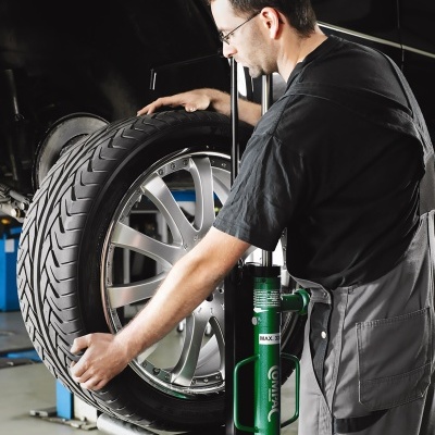 Homem a manusear pneu com jante de liga leve prata numa oficina mecânica