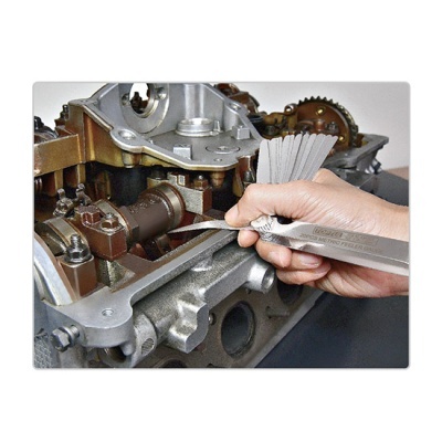 Mão a medir folgas numa peça de motor metálica com calibrador