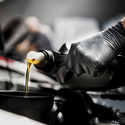 Luva preta a verter óleo de recipiente para funil numa oficina