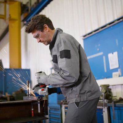 Homem a usar equipamento de proteção cinzento a trabalhar numa rebarbadora numa oficina industrial