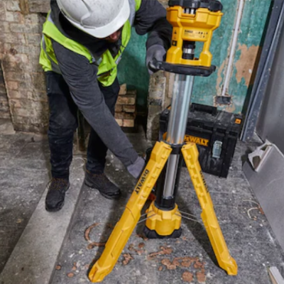 Tripé amarelo com ferramenta elétrica em construção e homem com colete e capacete
