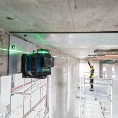 Laser de nível verde fixado em estrutura de betão com trabalhador em andaime ao fundo