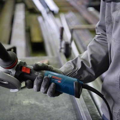 Pessoa a segurar rebarbadora elétrica Bosch azul num ambiente industrial