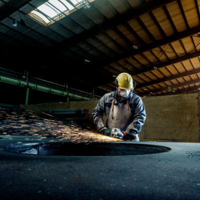 Trabalhador industrial usando capacete e máscara a esmerilhar superfície metálica