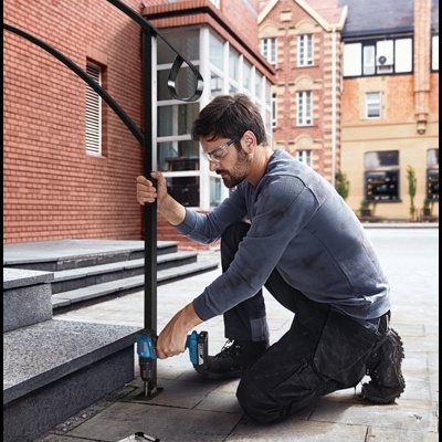 Homem a usar furadeira para fixar estrutura metálica negra no chão de pedra.