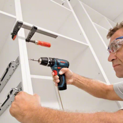 Homem a montar móvel branco com furadeira e óculos de proteção