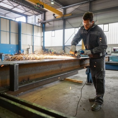 Homem a esmerilhar perfil metálico num atelier industrial