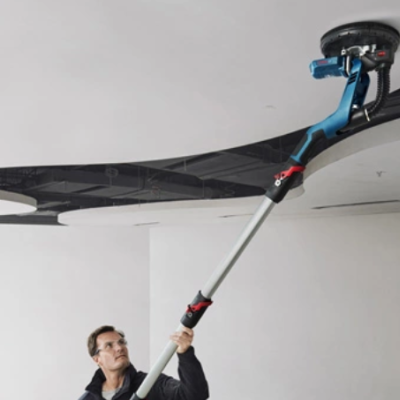 Homem com escova de limpeza eléctrica a limpar teto branco com decoração preta