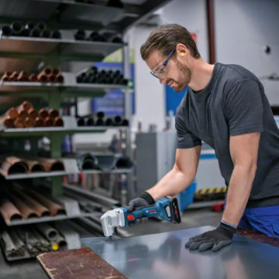 Homem a cortar chapa metálica com ferramenta elétrica numa oficina
