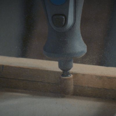 Impressora 3D imprimindo peça cilíndrica castanha numa estrutura de madeira clara.