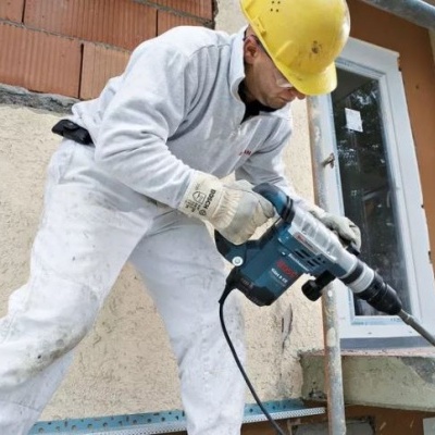 Homem com capacete amarelo a usar martelo perfurador azul e preto em parede exterior de edifício