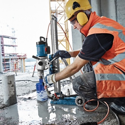 homem com colete refletor e capacete a operar máquina perfuradora numa obra