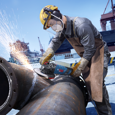 Trabalhador a usar rebarbadora para cortar tubagem metálica num cais industrial