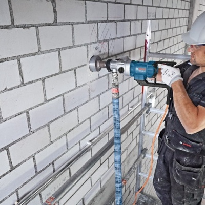 Operário a usar ferramenta elétrica para perfurar parede de tijolos