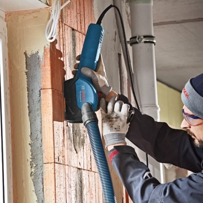Homem a usar máquina eléctrica azul para trabalho de construção em parede de tijolos