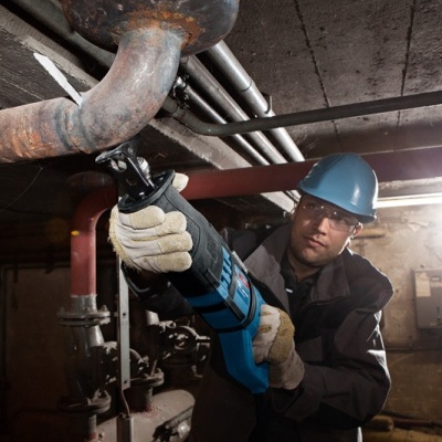 Homem a cortar tubo de metal com serra elétrica em ambiente industrial