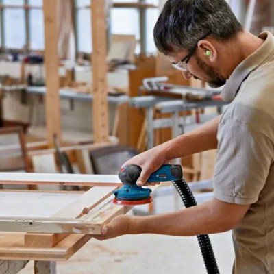 Homem a lixar madeira com lixadora elétrica numa oficina de carpintaria