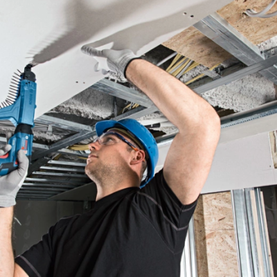 Trabalhador de construção a instalar placas de gesso no teto com furadeira azul