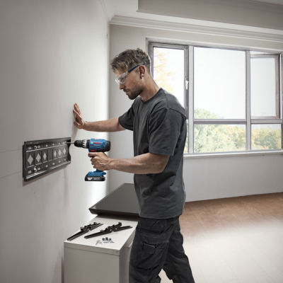 Homem a usar furadeira elétrica Bosch a fixar suporte metálico na parede branca