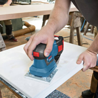 Lixadora elétrica azul a lixar placa branca numa oficina