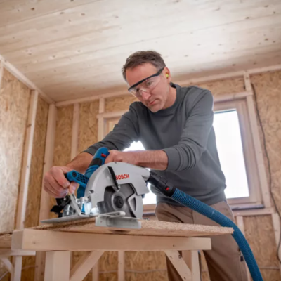 Serra circular Bosch azul e dourada em uso numa divisão em construção