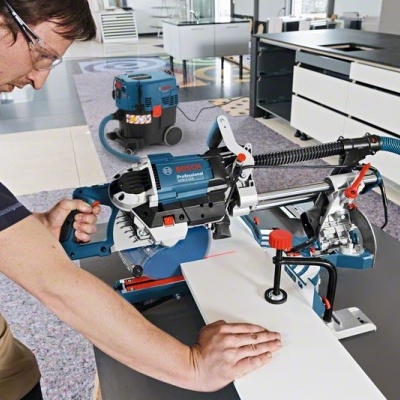 Serra de esquadria Bosch azul com tubo para pó em oficina manuseada por operário
