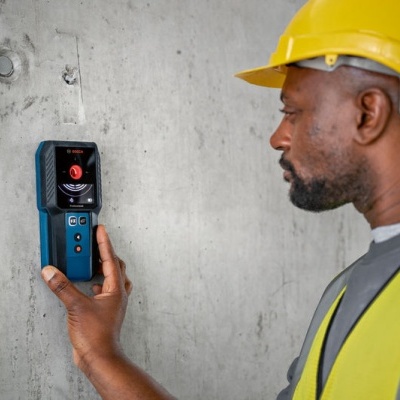 Homem com capacete e colete refletor usa dispositivo preso na parede