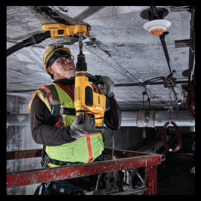 Trabalhador com furadeira amarela perfurando teto em ambiente industrial
