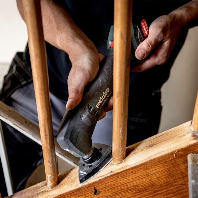 Pessoa a lixar corrimão de madeira com ferramenta Metabo em escada interior