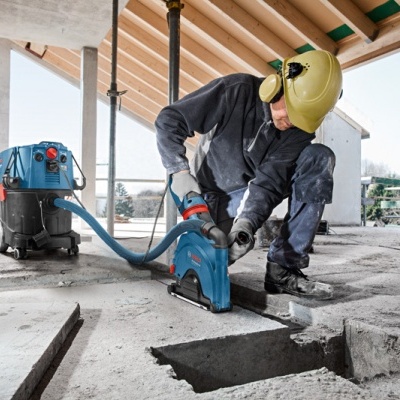 Trabalhador a usar ferramenta elétrica azul para cortar chão de betão numa construção
