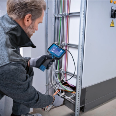 Homem a inspeccionar cabos elétricos com equipamento tecnológico numa caixa elétrica