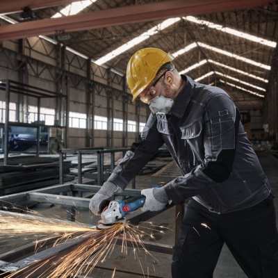 Homem com equipamento de proteção a cortar metal com rebarbadora elétrica em ambiente industrial