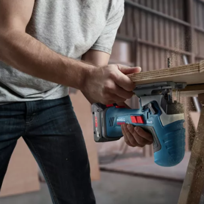 Homem a cortar madeira com ferramenta elétrica numa oficina