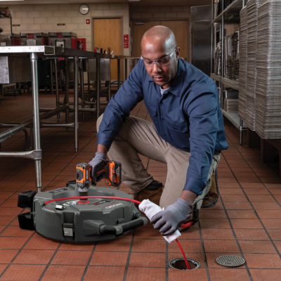 Homem a usar ferramenta cinzenta e sonda vermelha numa cozinha industrial.