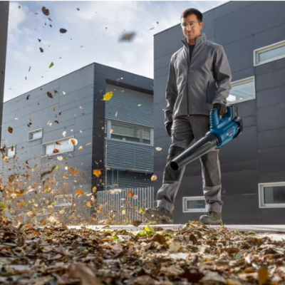 Homem com soprador de folhas a limpar folhas secas em área urbana moderna