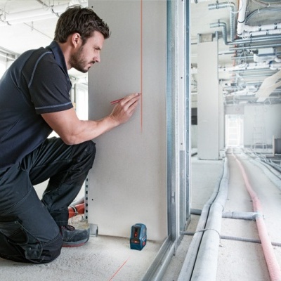 Homem a medir uma parede branca num espaço interior em construção