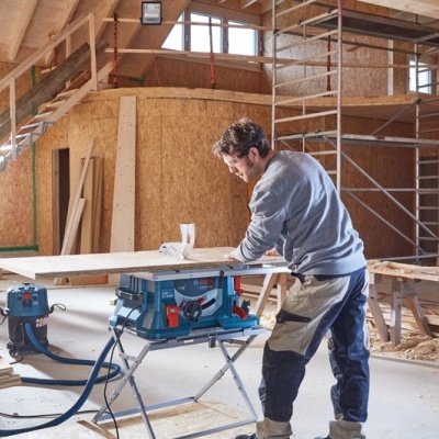 Oficina de carpintaria com homem a trabalhar e serra de esquadria azul
