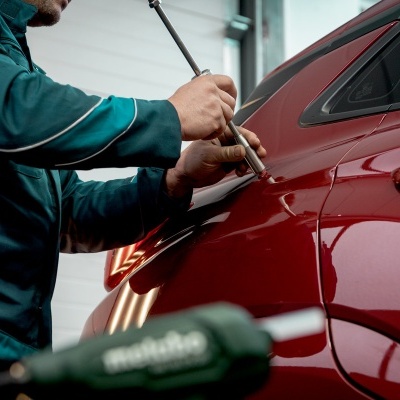 Pessoa a aplicar ferramenta em automóvel vermelho numa oficina