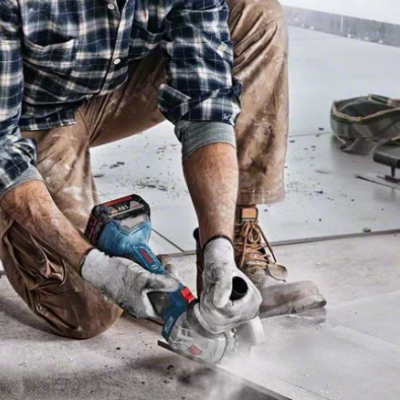 Homem a usar ferramenta elétrica para cortar placa branca em ambiente de obra