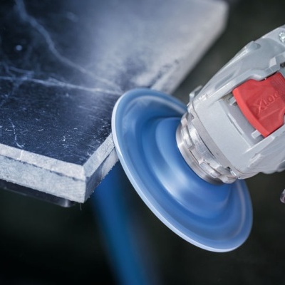 Esmerilhadora elétrica a desbastar pedra negra com disco abrasivo azul.