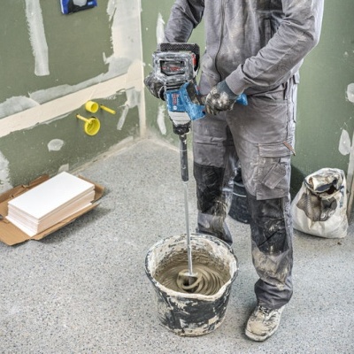 Homem a misturar pasta em balde no chão de obra com paredes verdes e chão cinzento