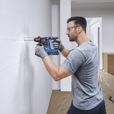 Homem a usar furadeira Bosch numa parede branca em ambiente interno com escada e chão protegido