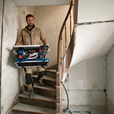 Homem a descer escadas de construção a transportar caixa azul Bosch com ferramentas