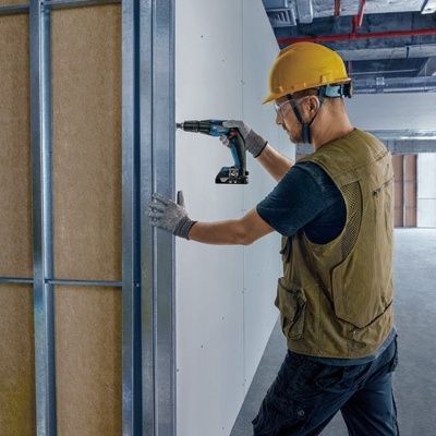 Trabalhador com capacete e colete a usar furadeira para fixar placa branca em estrutura metálica