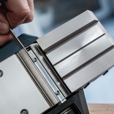 Mão a ajustar peça metálica prateada com ferramenta pequena