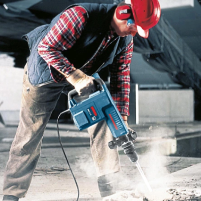 Trabalhador de construção a usar furadeira elétrica azul em obra com capacete vermelho